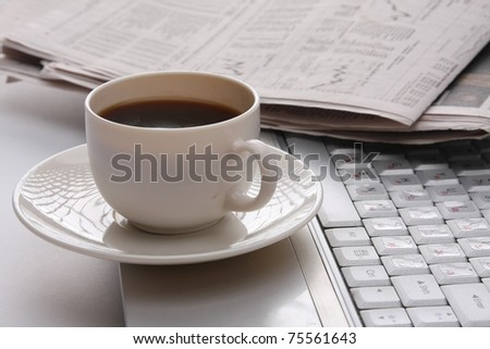 A cup of coffee and a newspaper on a laptop