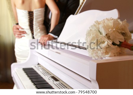 A bride and a groom near a white piano, focus on the flower bunch
