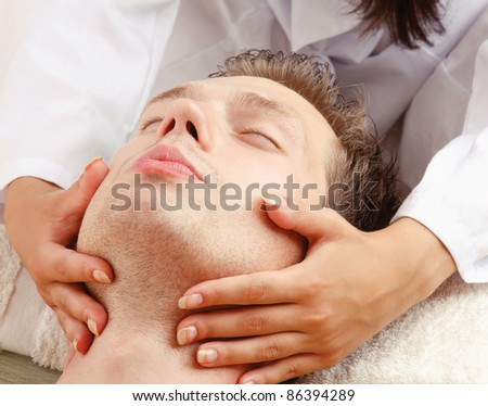 Close-up of relaxed young man getting facial massage isolated