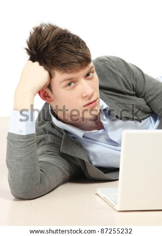 A young college guy lying on the floor with a laptop, isolated on white