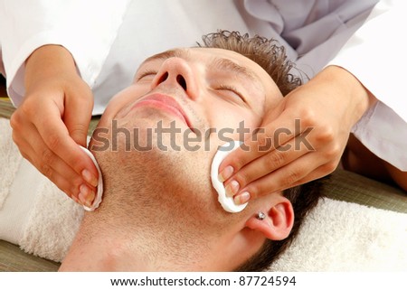 Female hands cleaning man\'s face with cotton swabs in a spa center