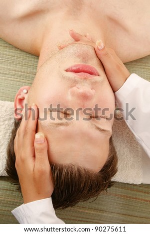 A female hands massaging man\'s face in a spa center