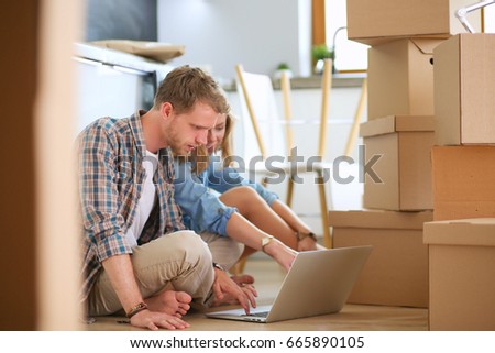 Young couple moving in new home.Sitting on floor and relaxing after unpacking.Looking something on laptop