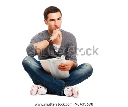 A full-lenght portrait of a young handsome college guy sitting on the floor and studying, isolated on white