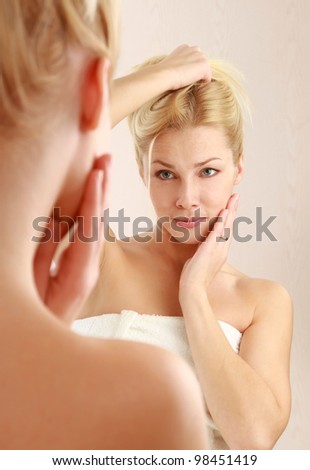 Woman caring of her beautiful skin on the face standing near mirror