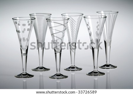 Six empty etched crystal liqueur glasses, with a gray background.