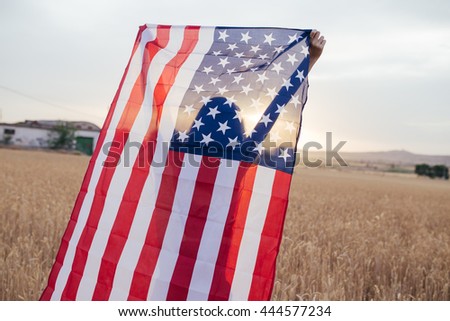 Girl with american flag smiling in the sunset. Young woman playing with USA flag in the 4th of July.