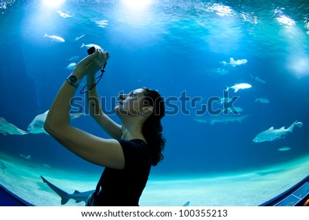Woman taking pictures of fish in front of aquarium.