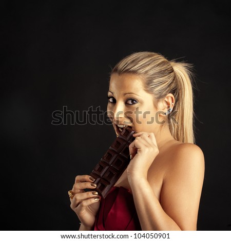 Beautiful woman with golden make up eating chocolate against black background.