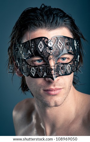 Close up portrait of young man with carnival mask against dark background.