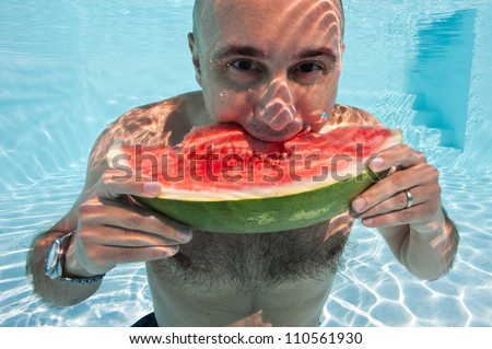 Underwater man eating a slice of watermelon in swimming pool.