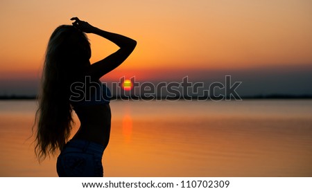 Beautiful young woman silhouette at the beach at sunset.