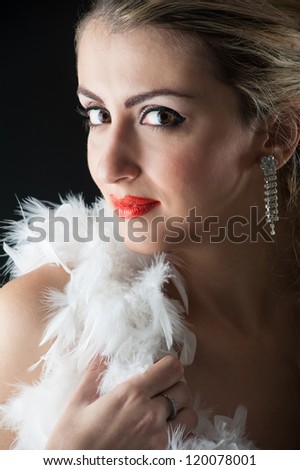 Beautiful blonde woman close up portrait with white ostrich feather against black background.