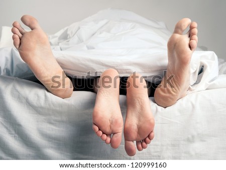 Couple having sex in bed under sheets.