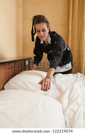 Chambermaid woman changing sheets in a hotel room.