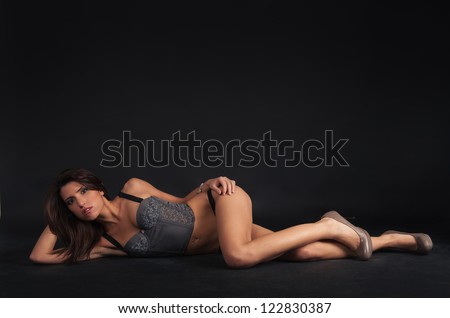 Sexy woman portrait wearing top corset and lying down against dark background.