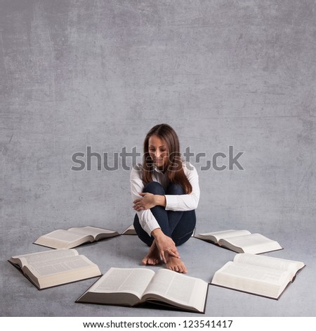 Young girl studying surrounded by books against grey background with copy space.