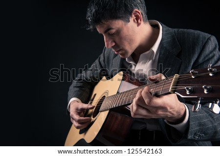 Man playing guitar against black background. Focus on hand.