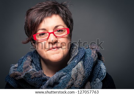 Middle age woman with red glasses close up portrait on dark background.