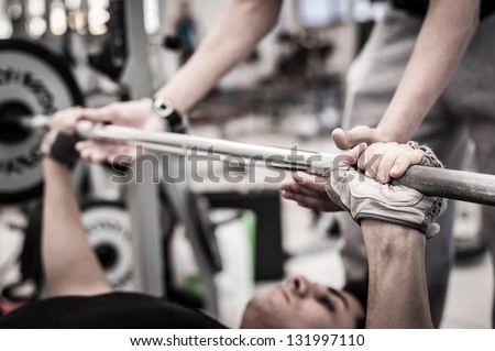 Young Man Lifting The Barbell In The Gym With Instructor. Focus On Hand.