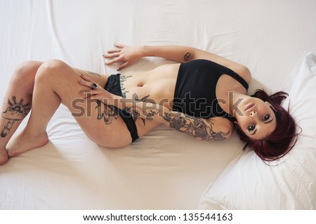 Sensual portrait of beautiful girl with tattoo lying on bed.