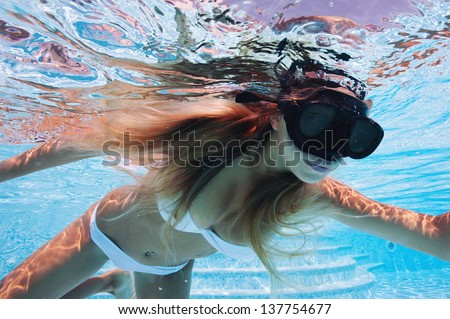 Underwater woman wearing mask with white bikini in swimming pool.