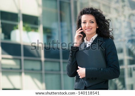 Business woman portrait outdoors talking at the phone with modern building as background.