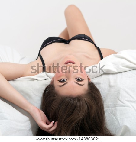 Portrait of a sensual young woman lying in bed upside down.