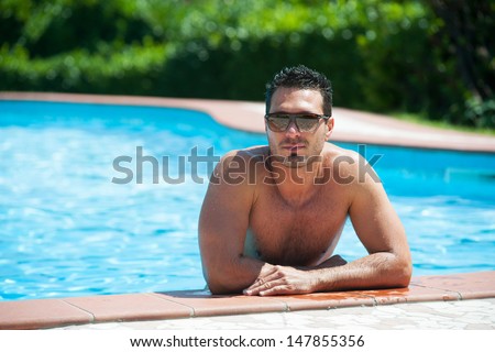 Portrait of a handsome and happy man relaxing at the side of a sun bathed swimming pool.