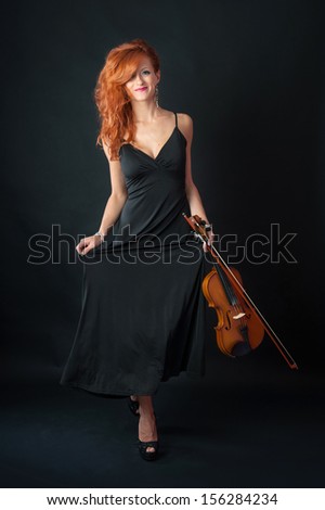 Young woman with violin against black background. Full body portrait.