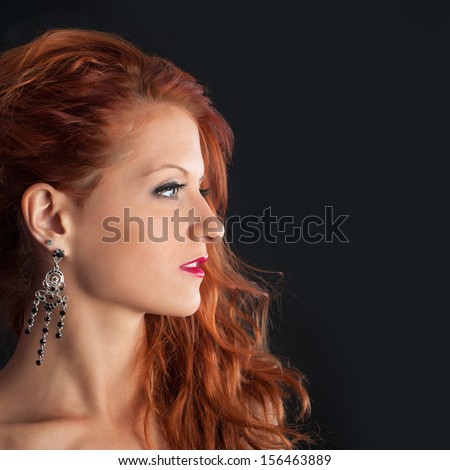 Young redhead woman profile portrait against black background.