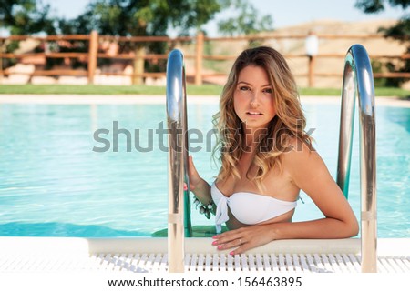 Beautiful woman portrait wearing white bikini posing by swimming pool.