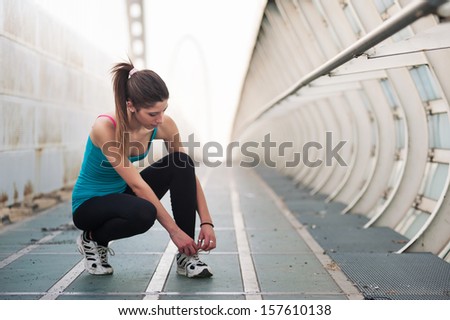 Young woman lacing her shoes outdoors on a modern bridge. Workout wellness concept.