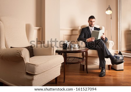 Young businessman relaxing reading a book sit on armchair.