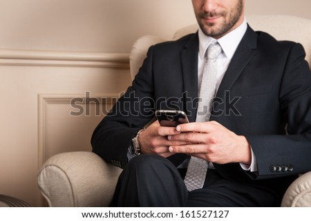 Young Businessman Sending Message With Mobile Phone Sit On Armchair.