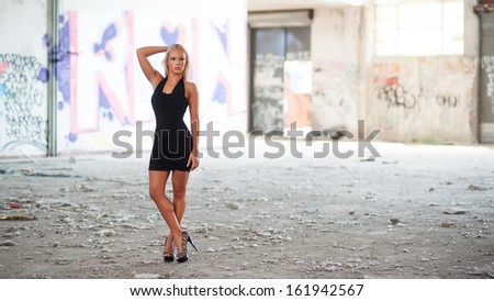 Sensual blonde woman portrait with black dress inside abandoned factory. Full body.