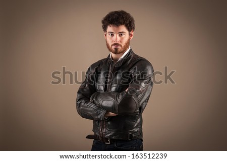 Portrait of confident young man wearing leather jacket against brown background.