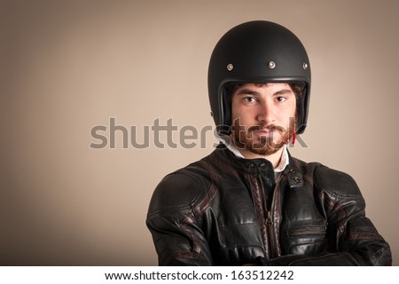 Portrait of confident young man wearing leather jacket and helmet against brown background.