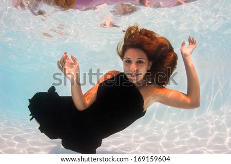 Underwater woman fashion portrait with black dress in swimming pool.