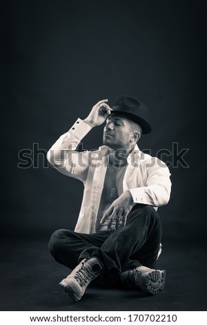 Man portrait playing with hat against dark background. Black and white image.