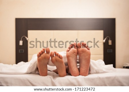 Couple relaxing in hotel room under sheets. Close up on feet.