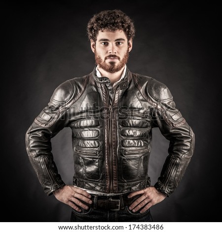 Portrait of confident young man wearing leather jacket against black background.