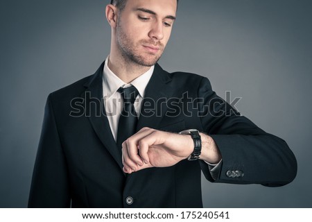 Businessman looking at the time on his wrist watch against dark background.
