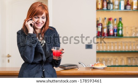 Young redhead woman portrait while talking at the phone inside a hotel bar.