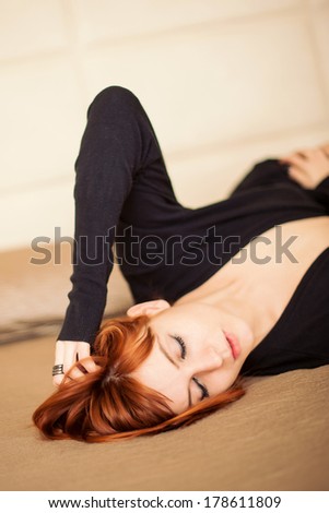 Sensual young red head woman portrait while lying on bed in hotel room. Shallow depth of field.