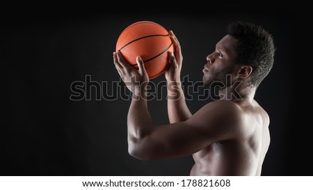 Portrait of confident young black man shirtless throwing basket ball against black background.