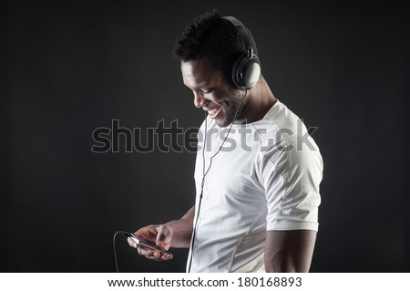 Black man listening to music with ear-phones against dark background.