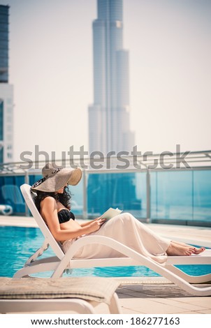 Young woman portrait relaxing and reading a book in swimming pool in Dubai. Filtered image.