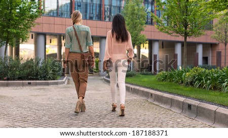 Young women couple walking portrait from behind outdoors in a park.