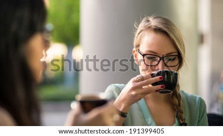 Young blonde woman drinking coffee with friend in a cafe outdoors. Shallow depth of field.